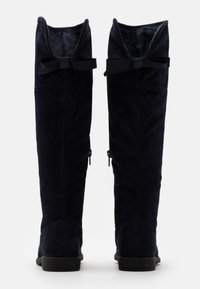 Bottes hauteur cuisse en daim bleu marine avec intérieur doux, ornées d'un nœud en haut et fermeture éclair latérale. Semelle plate.