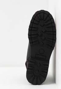 Bota Timberland negra con una suela gruesa de goma texturizada que presenta profundas ranuras y un logo. El lateral es liso con detalles de costuras visibles.