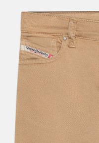Vaqueros de mezclilla beige con un bolsillo frontal con una etiqueta de Diesel Industry, herrajes plateados y una textura sutil. Corte clásico sin adornos visibles.