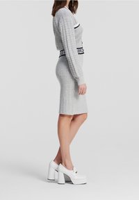 Szary dzianinowy komplet dwuczęściowy z krótkim topem z długim rękawem i dopasowaną spódnicą do kolan; posiada kontrastowe czarno-białe paski. Białe buty na platformie.