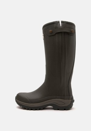 Stivale alto di gomma marrone scuro con suola zigrinata e cinturino decorativo vicino alla parte superiore su uno sfondo semplice.