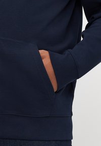 Sweat-shirt bleu marine avec une poche kangourou, des poignets et un ourlet côtelés. Le tissu semble lisse avec une finition légèrement texturée.