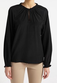 Blouse noire à manches longues avec un col froncé et une découpe en forme de trou de serrure. Les manches se resserrent aux poignets, offrant une coupe ample et une texture lisse.