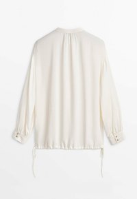 Blouse blanche à manches longues avec empiècement froncé dans le dos, poignets boutonnés et cordons réglables à l'ourlet.