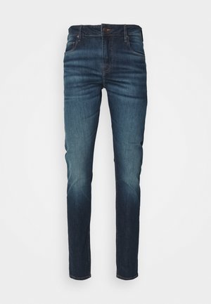 Jeans slim fit denim di colore blu scuro con una finitura sbiadita. Materiale: misto cotone. Presentano cinque tasche e una chiusura a bottone.