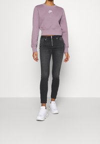 Sudadera recortada púrpura con logo blanco, combinada con jeans skinny negros con cremallera y zapatillas deportivas blancas.