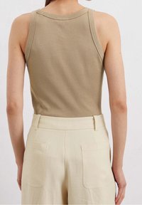 Top sin mangas color beige con escote redondo, combinado con pantalones crema de cintura alta que cuentan con dos bolsillos traseros. Tela suave y lisa.