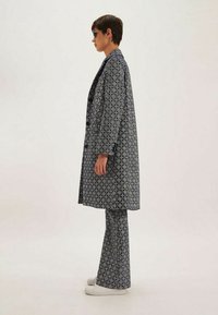 Ensemble imprimé en deux pièces bleu marine et blanc, comprenant un long manteau et un pantalon évasé avec des motifs géométriques et une texture lisse.