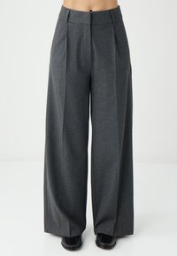 Kolen-grijze wijde broek met een textured stof, met voorplooien en een hoge taille. Zwarte schoenen completeren de look.