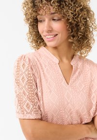 Light pink blouse with a textured diamond pattern, short puffed sleeves, and a V-neckline. Soft fabric with lace accents.