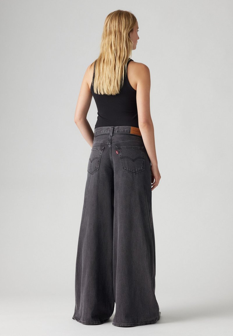 Weite schwarze Jeans mit ausgewaschenem Look, hoher Taille und Lederpatch auf der Gesäßtasche, ausgestattet mit traditioneller Naht und bequemer Passform.