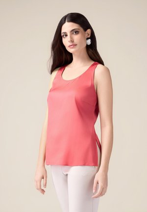 Top in satin corallo, presenta uno scollo a giro, taglio aderente, spacchi laterali e una texture liscia. Abbinato a leggings chiari.