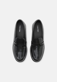Mocassins noirs en cuir avec un motif crocodile texturé, un bout lisse et un discret détail de logo sur la bride. Design classique à enfiler.