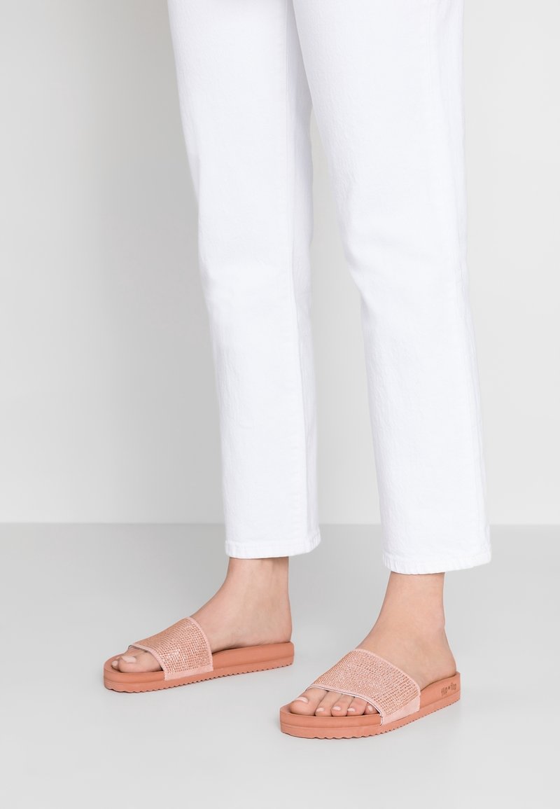 Sandales à bout ouvert en rose clair avec une sangle texturée et une semelle en caoutchouc épaisse, mises en valeur avec un pantalon blanc cropped.