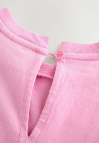 Približen posnetek roza izreza oblačila z rebrastim ovratnikom, ki ima zanko in gumb z majhnim okroglim roza gumbom.