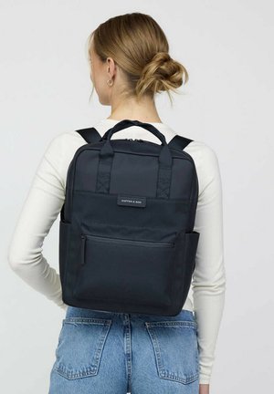 Zwarte nylon rugzak met verstelbare banden, twee zijzakken, een voorvak met rits en een handvat. Rechthoekige vorm met een minimalistisch ontwerp.