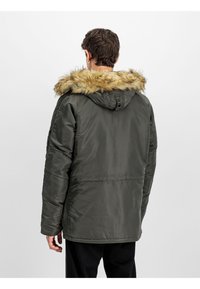 Chaqueta verde acolchada con capucha de piel sintética, que presenta una textura suave y un corte relajado. Costuras visibles y bolsillos a los lados.