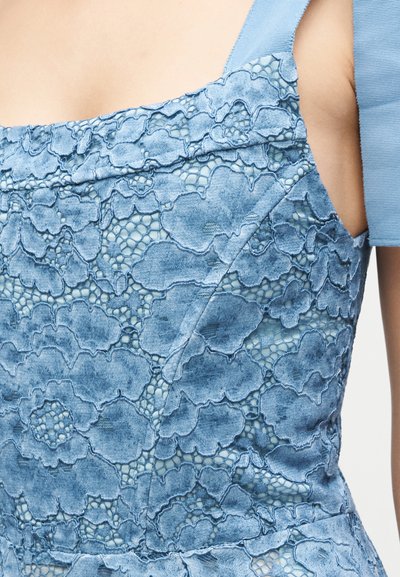 Κοντινό πλάνο μπλε δαντέλας φόρεμα που δείχνει λουλουδένια κεντήματα και δίχτυ ύφασμα με κοντό φουσκωτό μανίκι σε γυμνό πάνω χέρι.
