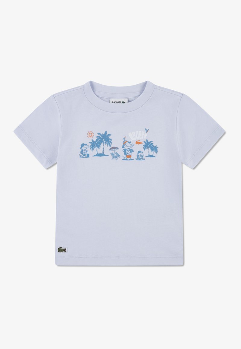 Ανοιχτό μπλε βαμβακερό μπλουζάκι με κοντά μανίκια. Στο μπροστινό μέρος υπάρχει γραφικό με φοίνικες, ήλιο και παιχνιδιάρικους χαρακτήρες. Λογότυπο Lacoste στο τελείωμα.