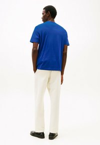 Blauwe katoenen T-shirt met een ronde hals, gecombineerd met crèmekleurige wijde broek en zwarte schoenen, van achteraf weergegeven. Eenvoudig ontwerp, geen patronen.