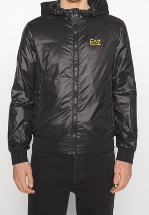 Zwarte glanzende gewatteerde jas met capuchon, voorrits, ritssluitingen aan de zijkanten, geribbelde manchetten en tailleband, en een geel "EA7 Emporio Armani"-logo op de borst.