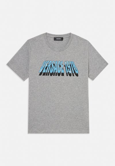Camiseta gris de manga corta con texto azul "VERSACE 1978" y sombra negra en el pecho, con cuello redondo.