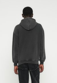 Tumehall suurte mõõtmetega kapuutsiga jope, millel on sile tekstuur, külge õmmeldud kapuuts ja soonilised varrukaotsad, kantud kulunud mustade teksadega.