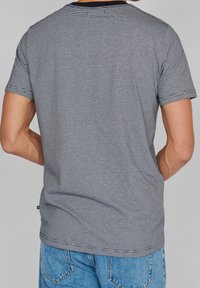 Grau gestreiftes T-Shirt mit kurzen Ärmeln, Rundhalsausschnitt und lockerem Schnitt. Der Stoff wirkt weich mit Nahtdetails und einem seitlichen Etikett.