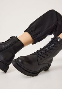 Black leather ankle boots with lace-up front, side zipper, and textured rubber sole, featuring stitching detail and smooth surface.