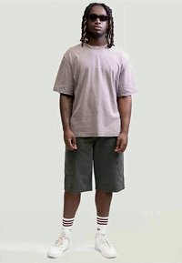 Γκρι υπερμέγεθες t-shirt, σκούρο πράσινο cargo σορτσάκι, λευκά αθλητικά παπούτσια με κόκκινες ρίγες και μαύρα γυαλιά ηλίου. Κοντό χτένισμα με πλέξη.