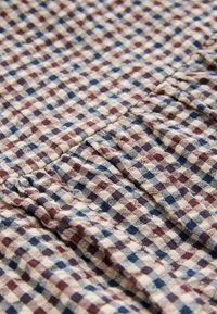 Tessuto a quadri con quadrati rossi, blu e beige di dimensioni variabili. Superficie testurizzata con leggero dettaglio di pieghe.