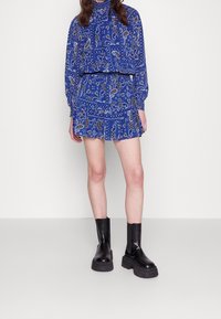 Conjunto de dos piezas de estampado azul que incluye una blusa de manga larga y una falda corta, combinado con botas de tobillo negras y brillantes.