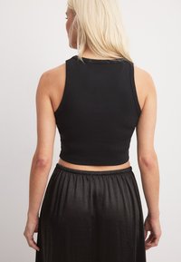 Črn rebrast top s krojem, ki poudari postavo, z širokimi naramnicami in robom brez obdelave, v kombinaciji z ohlapno črno krilo.