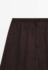 Jupe en tissu froissé marron foncé avec une ceinture élastique et une couture centrale à l'avant.