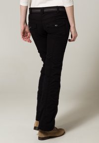 Pantalon noir au design ajusté, avec poches arrière, ceinture texturée et finition lisse. Stylisé avec des chaussures beige.