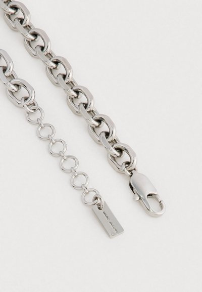 Strieborný reťazec s hrubými prepojenými článkami a karabínkou. Obsahuje malú visačku s názvom značky "Marc Jacobs."