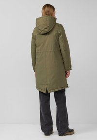 Olijfgroen gewatteerde jas met een capuchon en rugventilatie; heeft drukknoopsluitingen en een gladde textuur. Gecombineerd met donkere, wijde broeken.