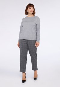 Maglione grigio a maniche lunghe con dettagli testurizzati abbinato a pantaloni grigi a quadri e décolleté nere a punta, creando un outfit strutturato.