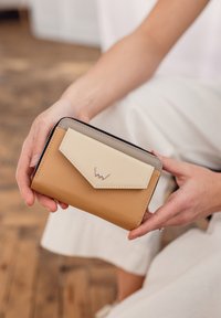 A three-tone wallet with a tan body and cream flap, featuring a gray accent and silver logo detail. Smooth leather texture with a zip closure.