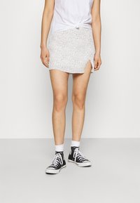 Mini-jupe blanche avec de petites taches noires, dotée d'une fente sur le côté, associée à des baskets montantes noires et des chaussettes blanches mi-mollet.