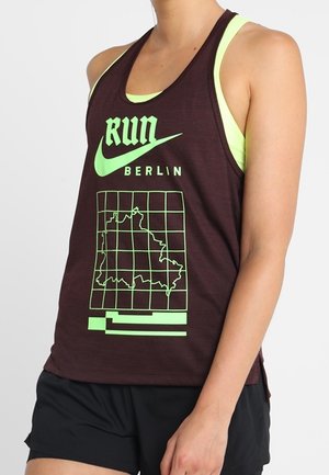 Atleet draagt een donker tanktop met neon groene "Run Berlin"-tekst, Nike-logo en kaartgrafiek, gecombineerd met zwarte korte broek.