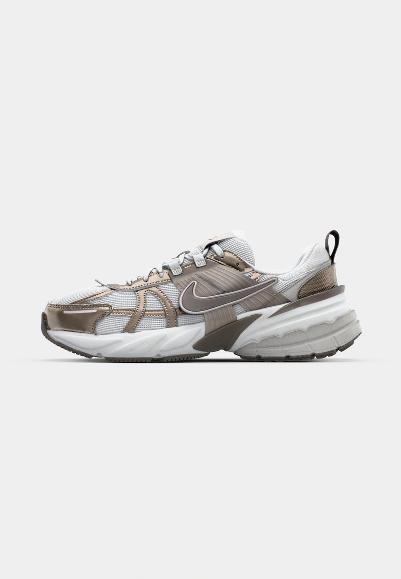 Zapatilla deportiva blanca y beige con materiales de malla y sintéticos, amortiguación prominente, sobrecapas texturizadas, sistema de cordones y detalle del logotipo.