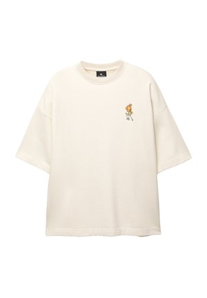 Krémové bavlnené oversized tričko s okrúhlym výstrihom, krátkymi rukávmi a malou farebnou výšivkou postavy na ľavej hrudi.