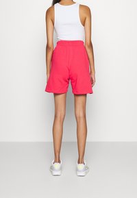 Růžové bavlněné šortky s uvolněným střihem a elastickým pasem, doplněné o bílé tenisky. Materiál se zdá být měkký a prodyšný.