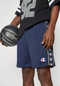 Sötétkék kosárlabdás rövidnadrág, könnyű anyagból készült, kontrasztos oldalsávokkal és logós részletekkel, kényelmes illeszkedéssel.