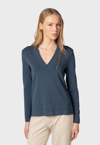 Tummansininen pitkähihaisuus pusero V-pääntiellä, valmistettu pehmeästä kankaasta. Ominaisuuksiin kuuluu rento istuvuus ja hillitty logo yksityiskohtana helmassa.