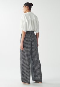 Blusa bianca a maniche corte abbinata a pantaloni larghi a righe in bianco e nero. I pantaloni presentano una vita alta e una vestibilità comoda.