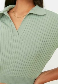 Haut en maille côtelée vert clair avec col et encolure en V, manches courtes et taille cintrée.