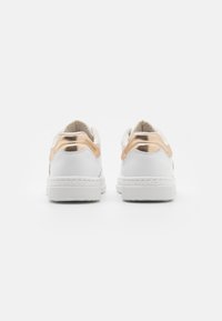 Baskets blanches avec un accent de talon en or rose métallique, texture en cuir lisse et semelle en caoutchouc avec un design perforé.