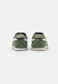 Zapatillas de tela verdes con acentos blancos, que cuentan con una puntera redondeada, cuello acolchado y talón con marca. Suela con tacos para mayor agarre.
